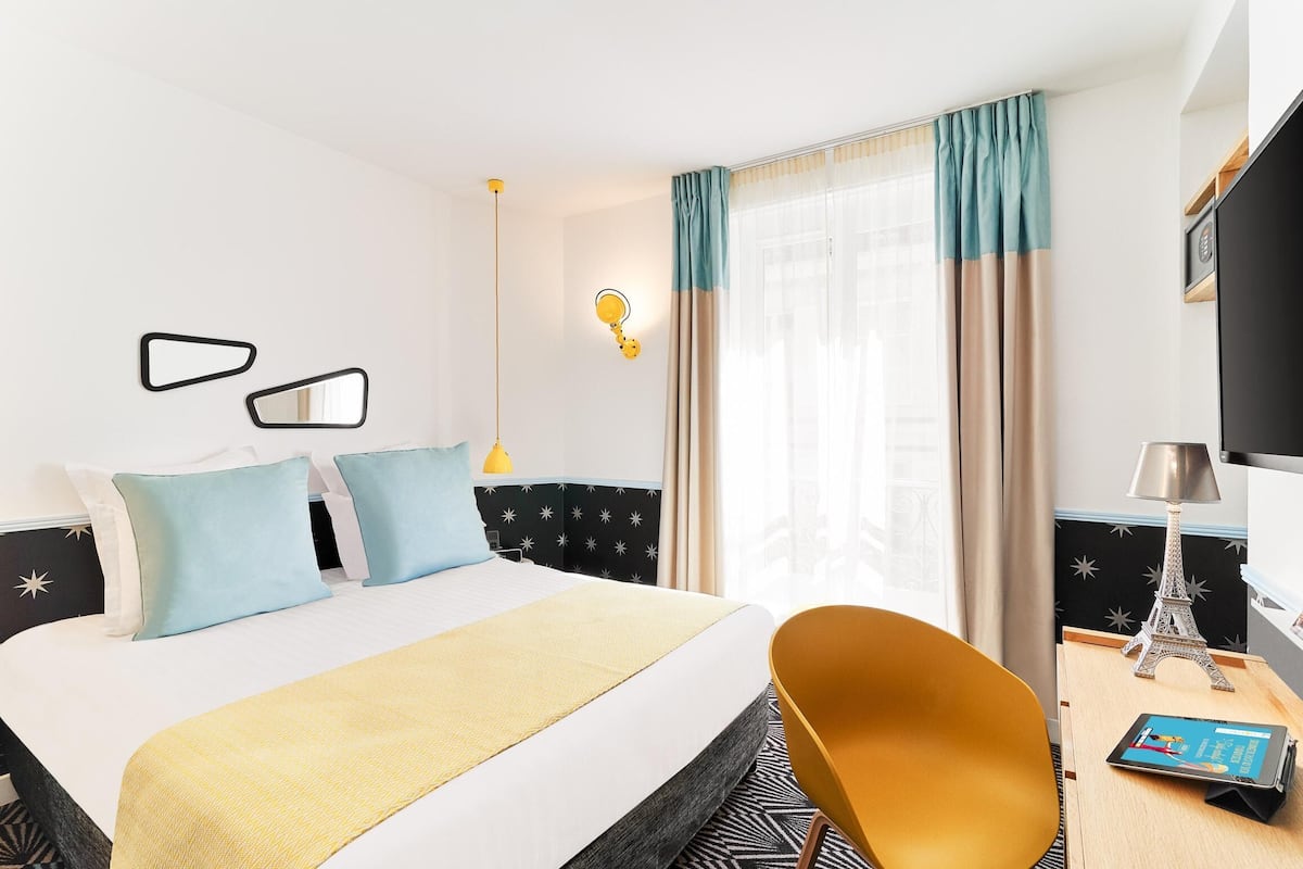 A hotel room with a bed, a desk with a lamp, and a chair.