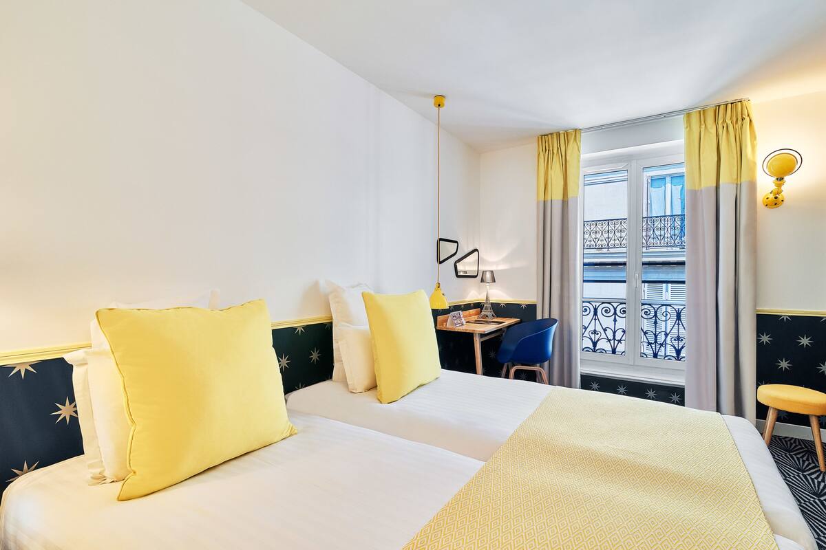 A hotel room with two beds, a desk, and a balcony with a railing.