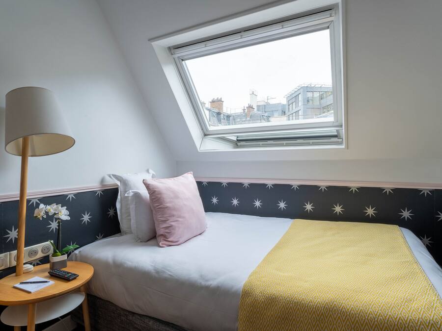A bedroom with a skylight, a bed with a yellow blanket, a bedside table with a lamp, and a nightstand with a plant.