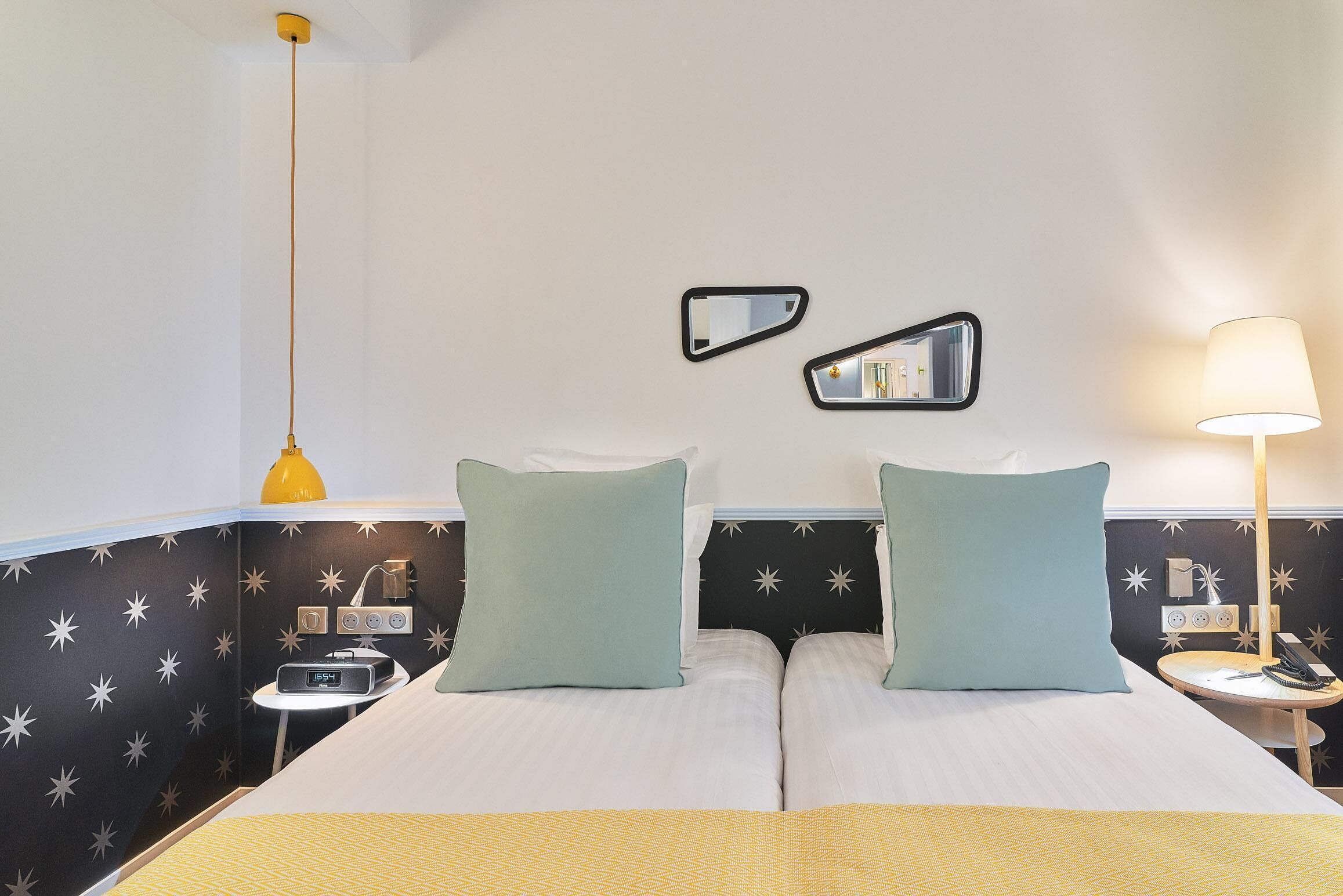 A double bed with two pillows, a bedside table with a lamp, a nightstand with a phone, and a wall clock.