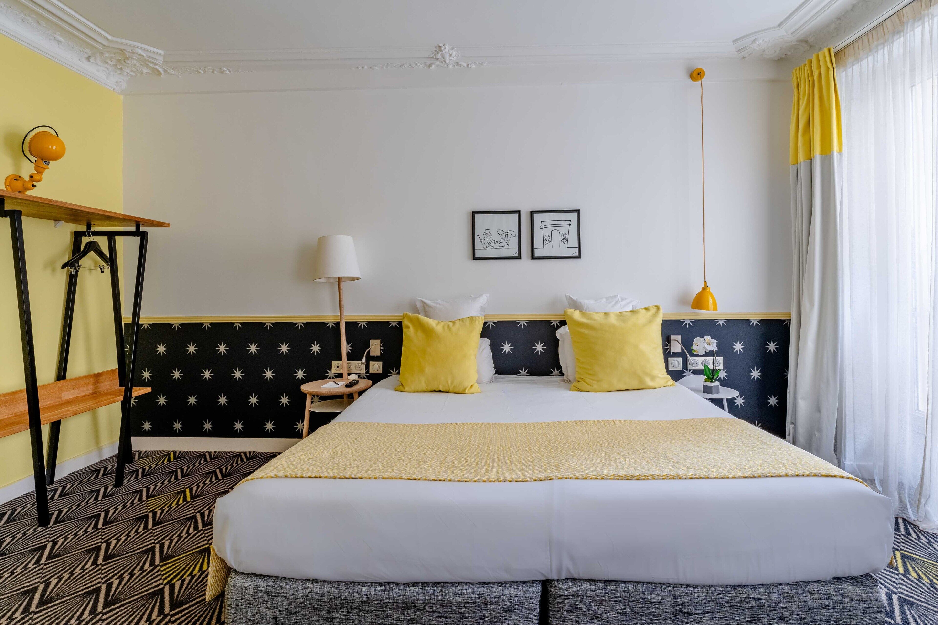 A hotel room with a large bed, two yellow pillows, a nightstand, a lamp, and a star-patterned headboard.