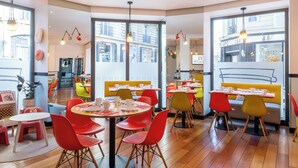 A brightly lit restaurant with colorful chairs and tables, large windows offering a view of the street, and a modern interior design. - Hôtel Augustin - Astotel (Paris)
