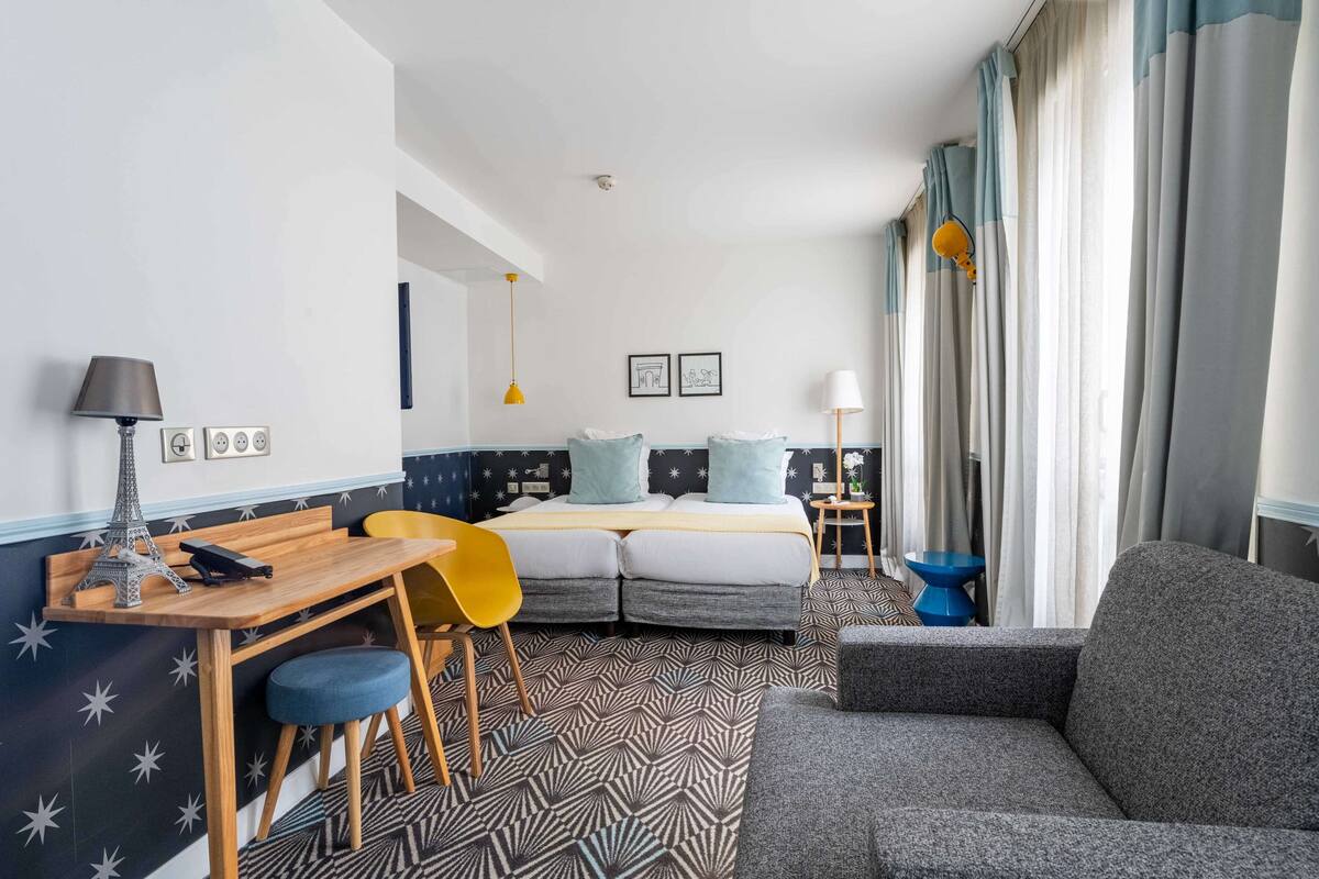 A modern hotel room with a bed, a desk, a chair, a sofa, and a small table.