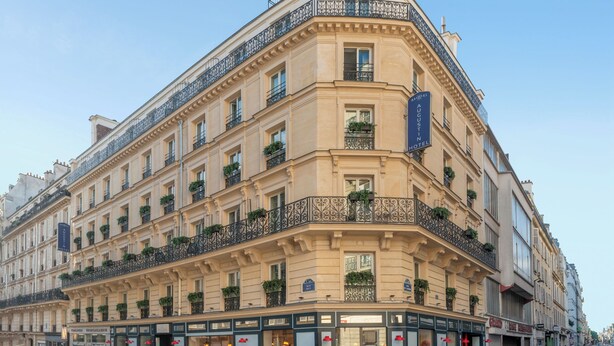 A multi-story hotel with a classic European architectural style, featuring balconies with wrought iron railings and potted plants. - Hôtel Augustin - Astotel (Paris)