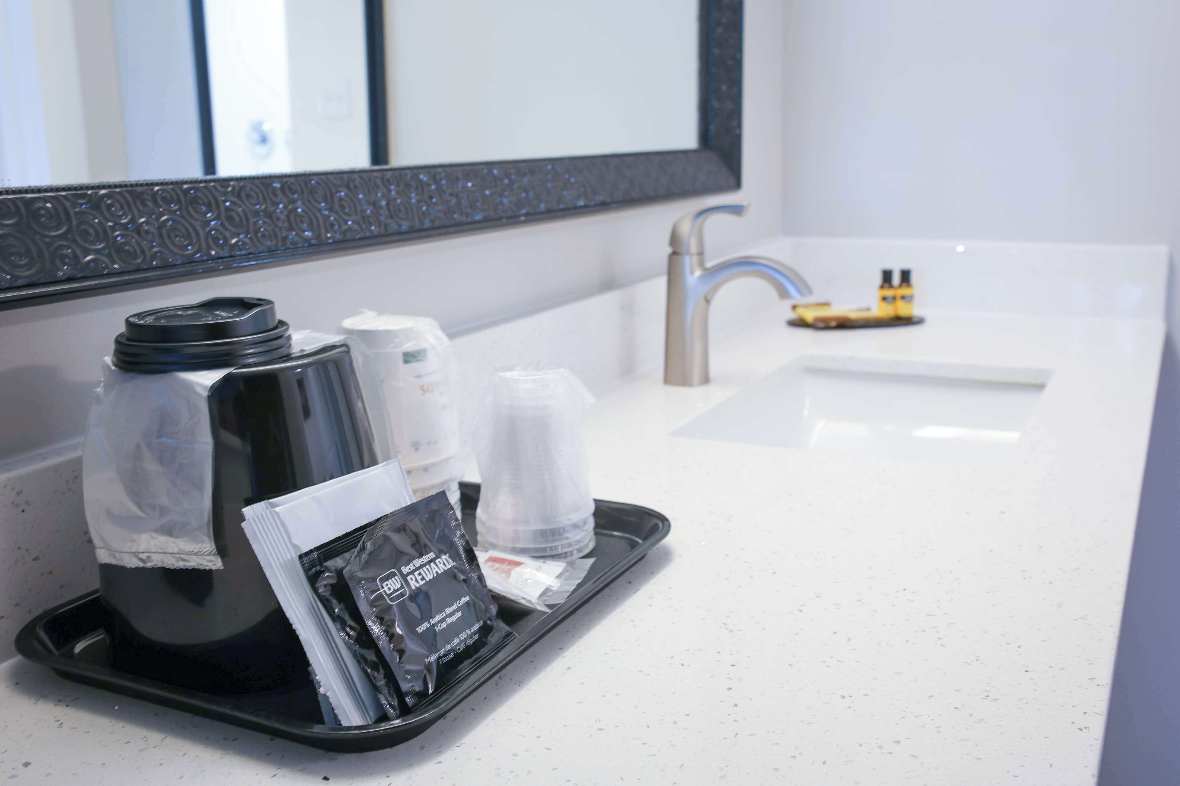 A tray with a coffee maker, a glass, and a packet of toiletries in a hotel bathroom.