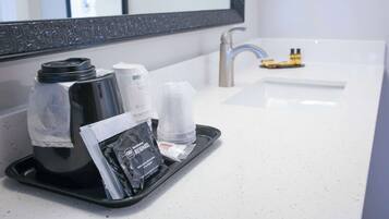 Una bandeja con cafetera, un vaso y artículos de aseo en un baño de hotel.