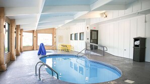 En inomhuspool med blå kakelplattor längs kanten, träpelare och en sittgrupp med gula stolar.