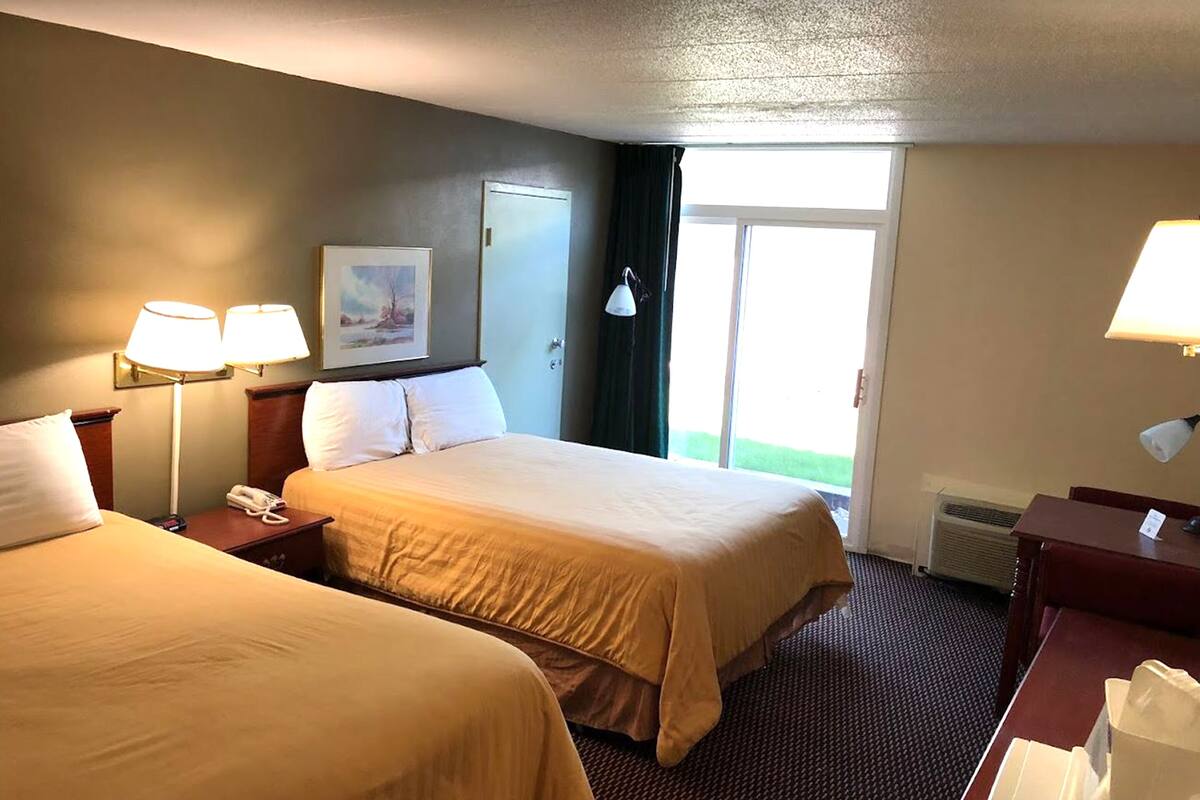 A hotel room with two beds, a painting on the wall, a door, and a window with a view.