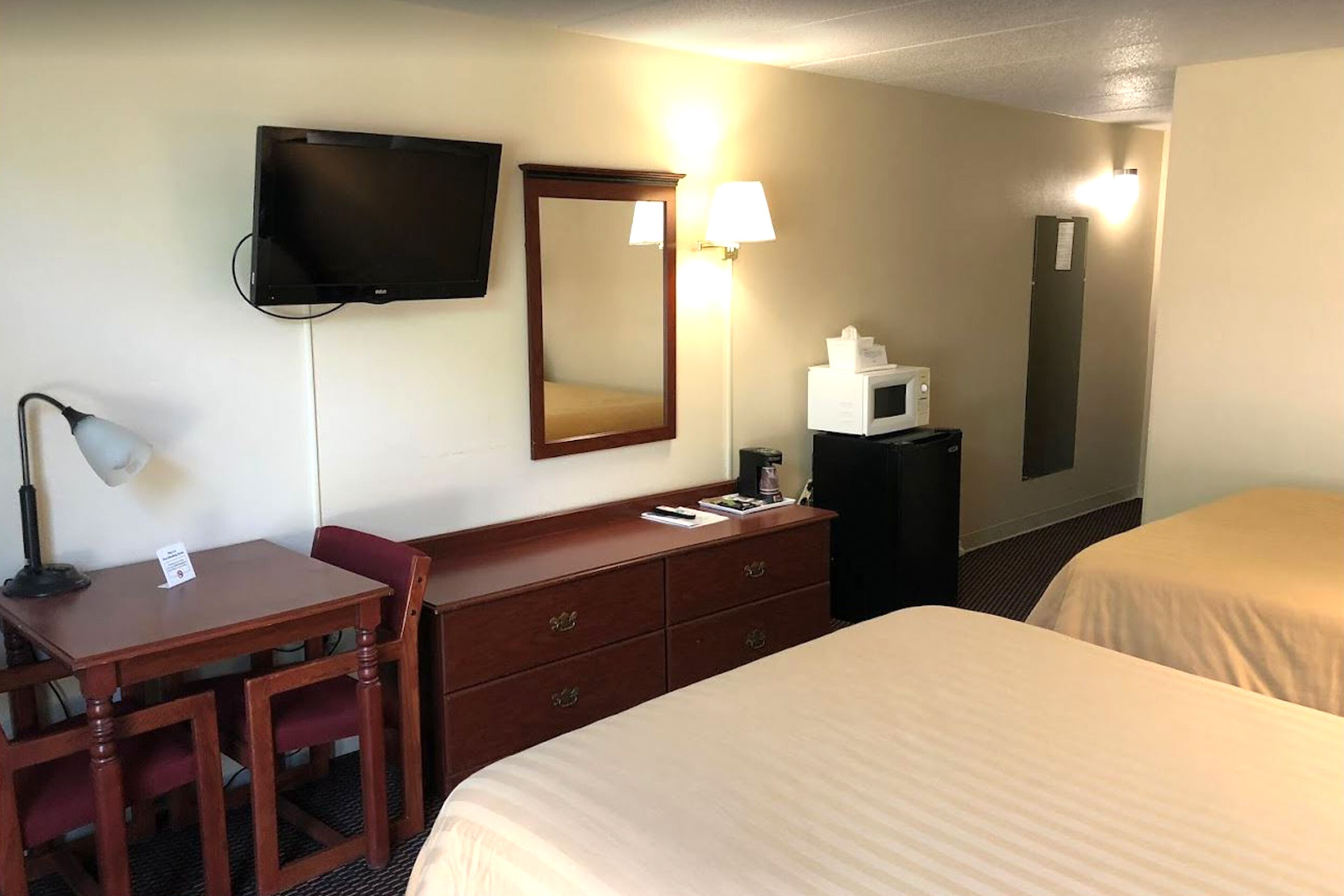 Quarto de hotel com escrivaninha, duas camas, televisão, espelho, micro-ondas e abajur.