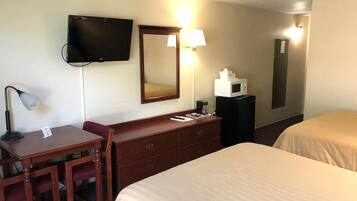 Quarto de hotel com escrivaninha, duas camas, televisão, espelho, micro-ondas e abajur.