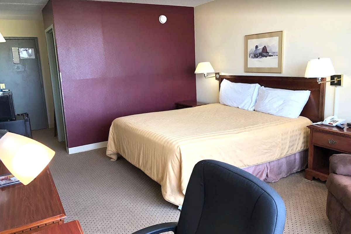A hotel room with a large bed, two bedside lamps, a desk with a lamp, a chair, and a framed picture on the wall.
