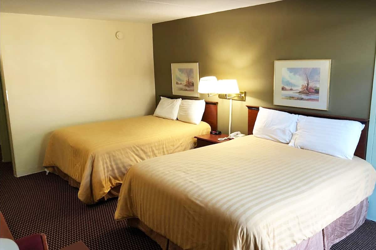 A hotel room with two beds, a nightstand with a lamp, and two framed pictures on the wall.