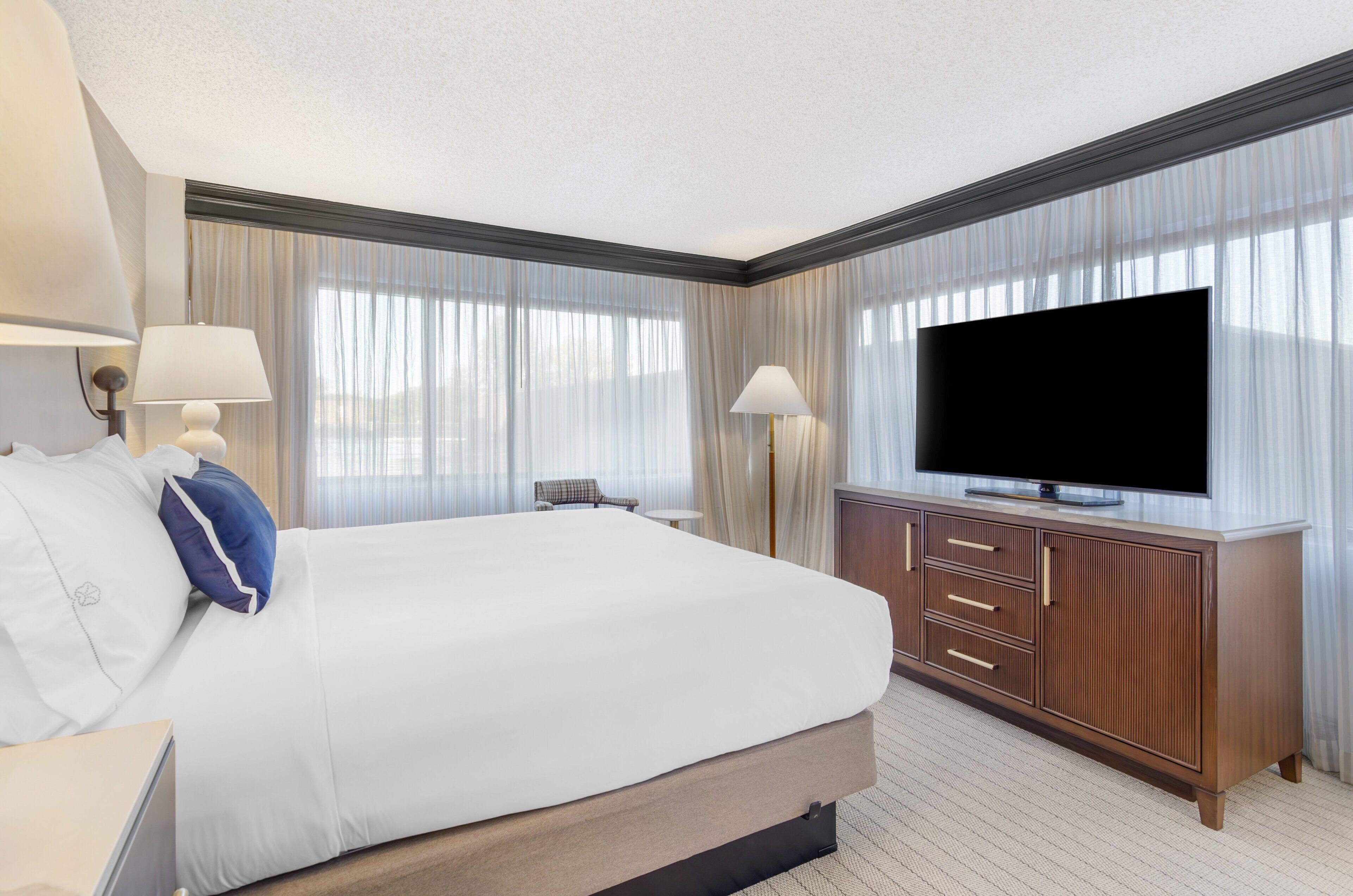 A hotel room with a large bed, a TV, a desk, and a chair.