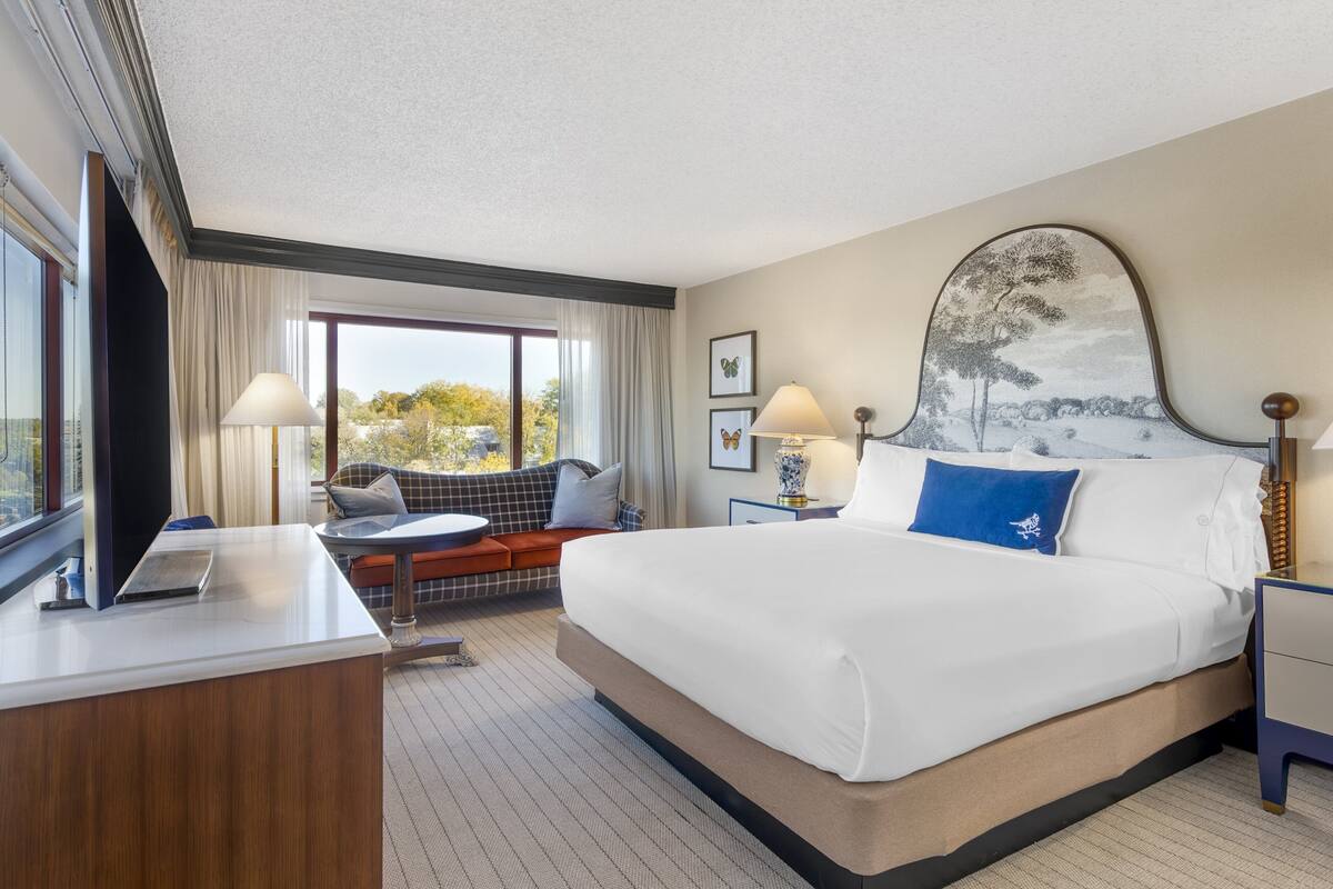 A hotel room with a large bed, a desk, a sofa, and a view of the outdoors.