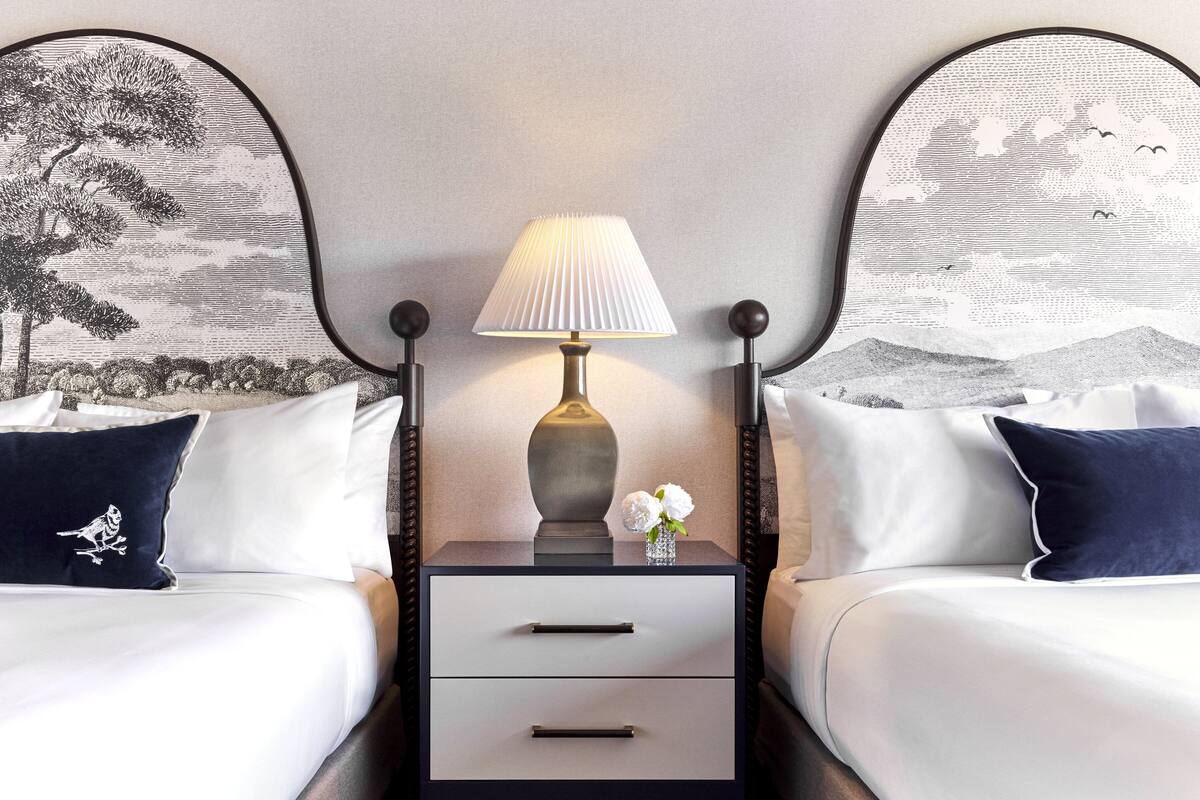 A hotel room with a bed, a nightstand with a lamp, and two wall-mounted headboards with landscape artwork.