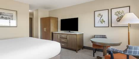 A hotel room with a bed, a TV on a wooden cabinet, a small table with a chair, and two framed pictures on the wall.
