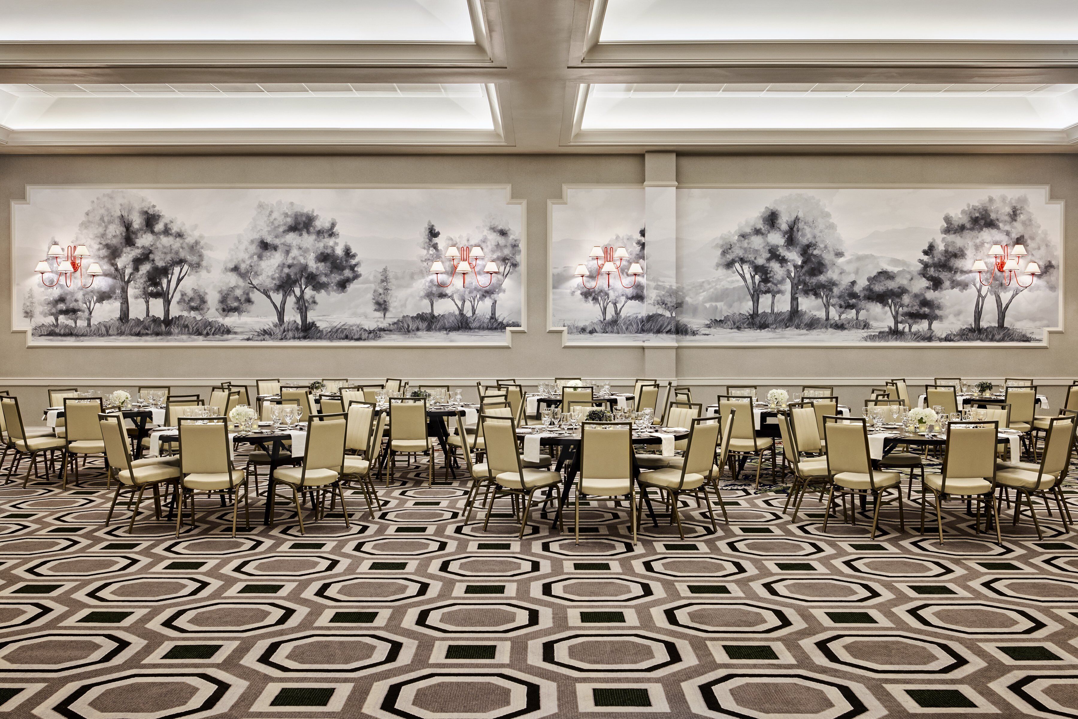 A banquet hall with round tables and chairs, large windows, and a geometric patterned carpet.