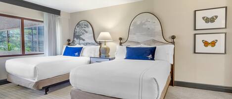 Habitación de hotel con dos camas, una mesita de noche, una lámpara y cuadros con mariposas en la pared.