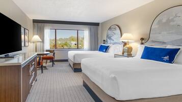 A hotel room with two beds, a desk, a TV, and a window with a view.