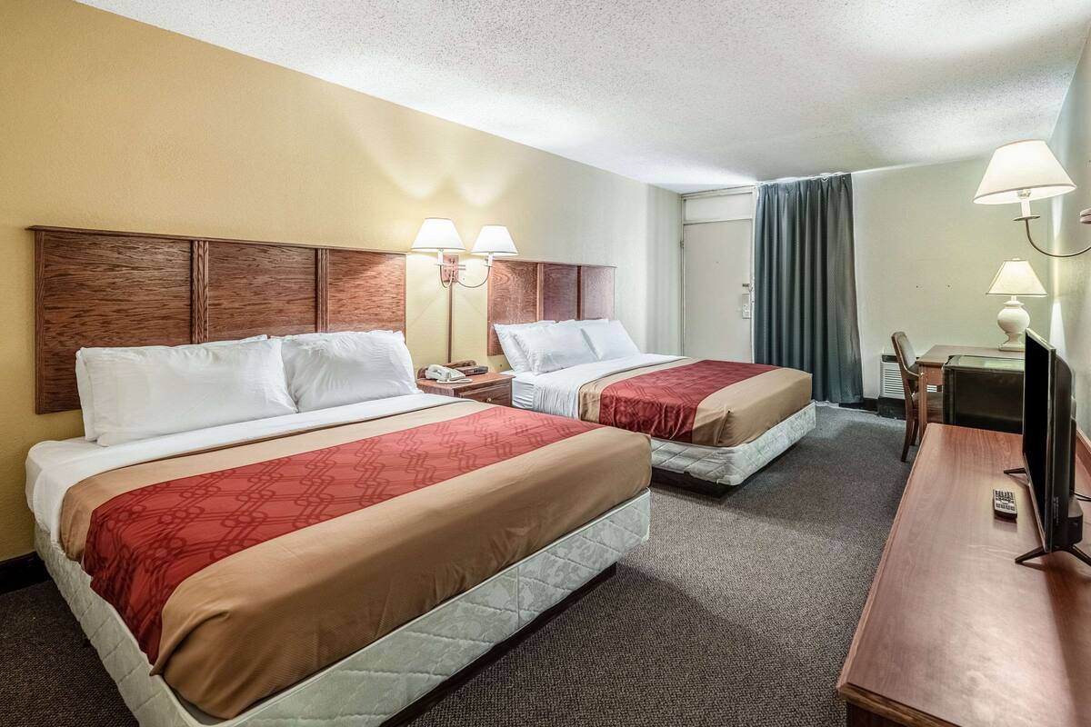 Ein Hotelzimmer mit zwei Betten, einem Schreibtisch, einem Sessel und einem Fernseher.