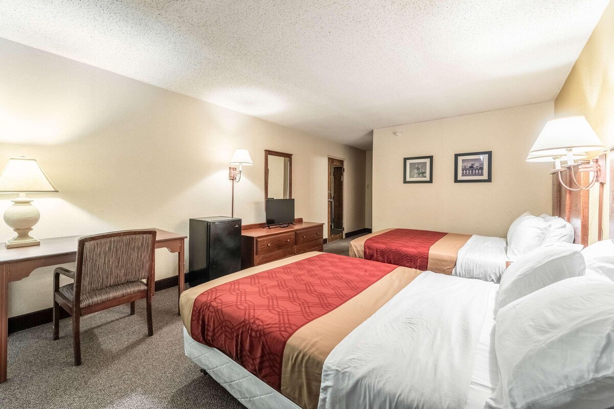A hotel room with two beds, a desk, a chair, a television, and a mirror.