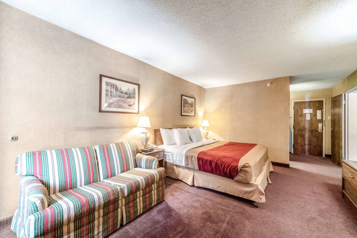 Ein Hotelzimmer mit Bett, gestreifter Couch, zwei Nachttischlampen und einem gerahmten Bild an der Wand.