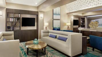 A modern living room with a sofa, armchairs, a coffee table, a flat-screen TV, bookshelves, and artwork on the walls.