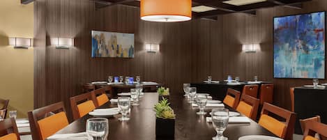 Un salón de conferencias con una larga mesa, sillas y una planta en maceta.