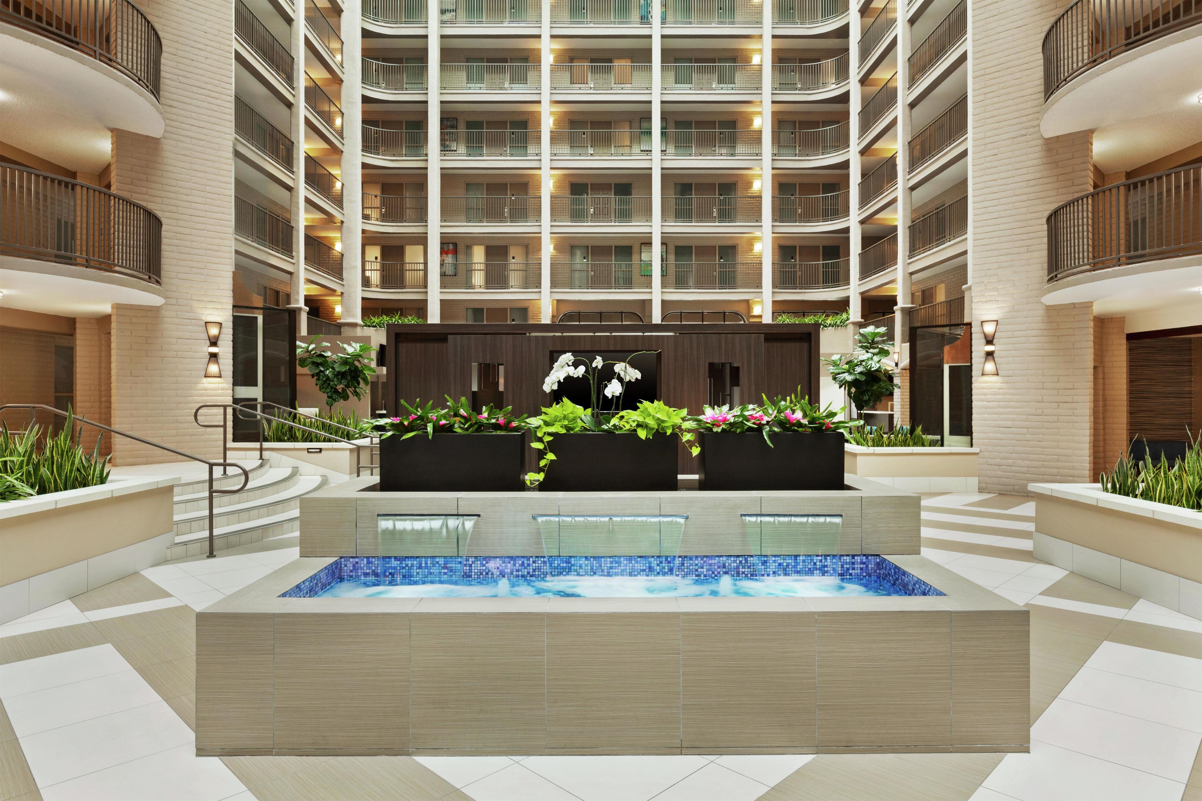 A modern hotel atrium with a central pool, multiple balconies, and indoor plants.