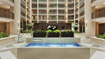 A modern hotel atrium with a central pool, multiple balconies, and indoor plants.