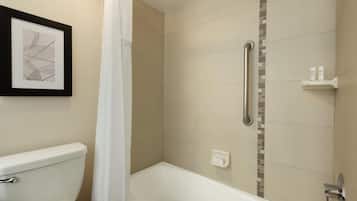 A bathroom with a bathtub, toilet, shower, and a framed picture on the wall.
