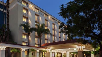 A multi-story hotel with a covered entrance, palm trees, and a red-tiled roof.