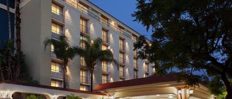 A multi-story hotel with a covered entrance, palm trees, and a red-tiled roof.