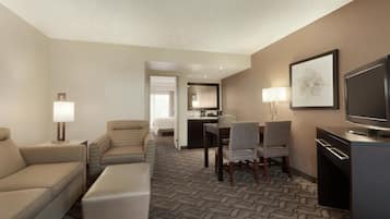 Habitación de hotel con sofá, dos sillones, una mesa de comedor con sillas, televisor y zona de cocina.