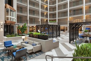 Un vestíbulo de hotel de varios niveles con zonas de estar, plantas y una escalera.