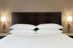 A hotel room with a large bed, two bedside lamps, and a dark headboard.