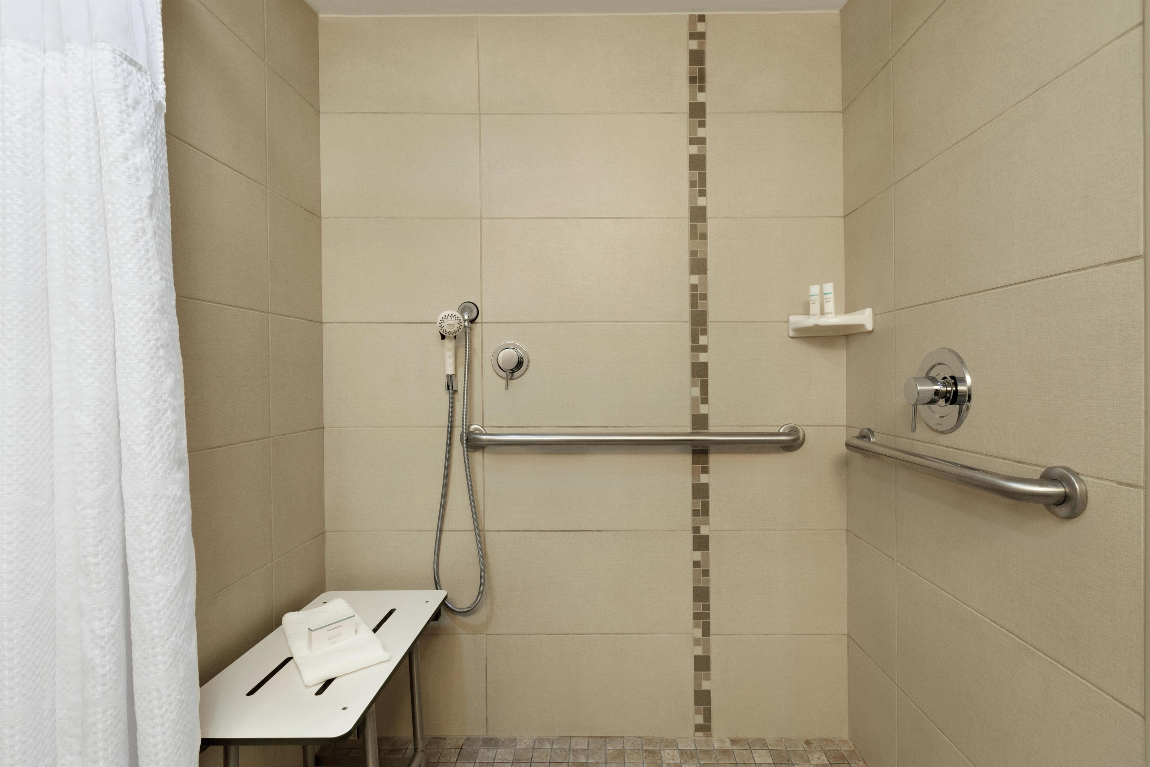 A shower with a grab bar, a white towel, and a shelf with toiletries.
