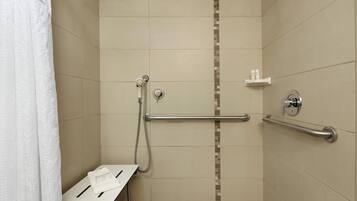 A shower with a grab bar, a white towel, and a shelf with toiletries.