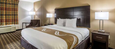 A hotel room with a large bed, two bedside tables with lamps, a chair, and a patterned carpet.