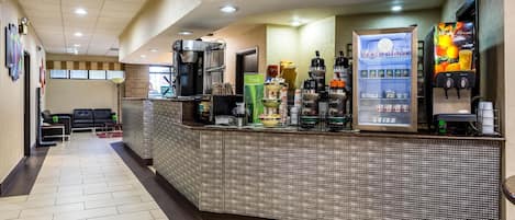 A hotel lobby with a coffee station, seating area, and a vending machine.
