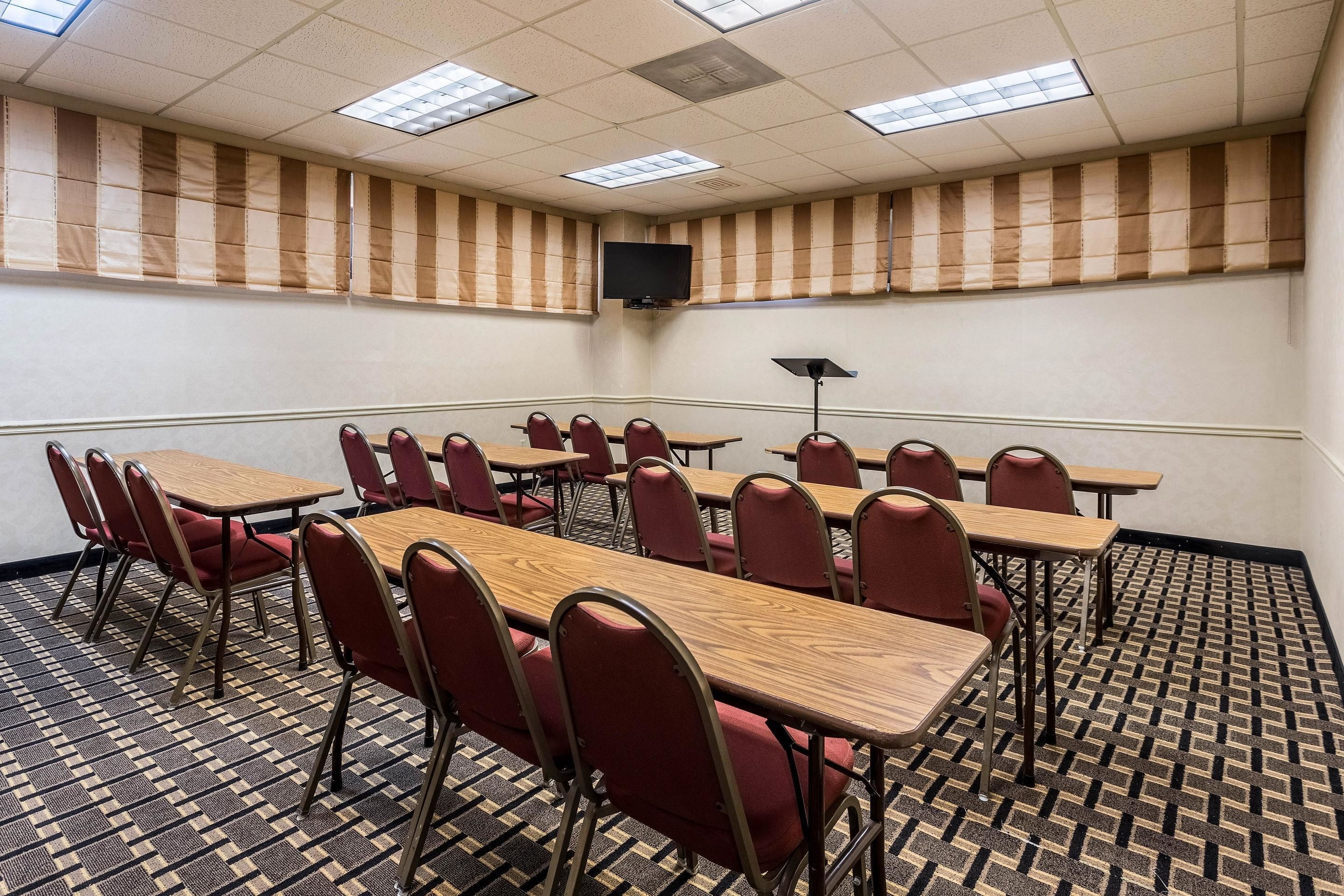 A conference room with multiple tables and chairs, a flat-screen TV mounted on the wall, and a patterned carpet.