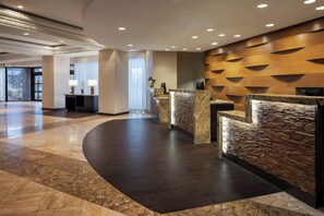 A modern lobby with a curved reception desk, a stone wall, and a large window allowing natural light. - Marriott Wichita (Wichita)