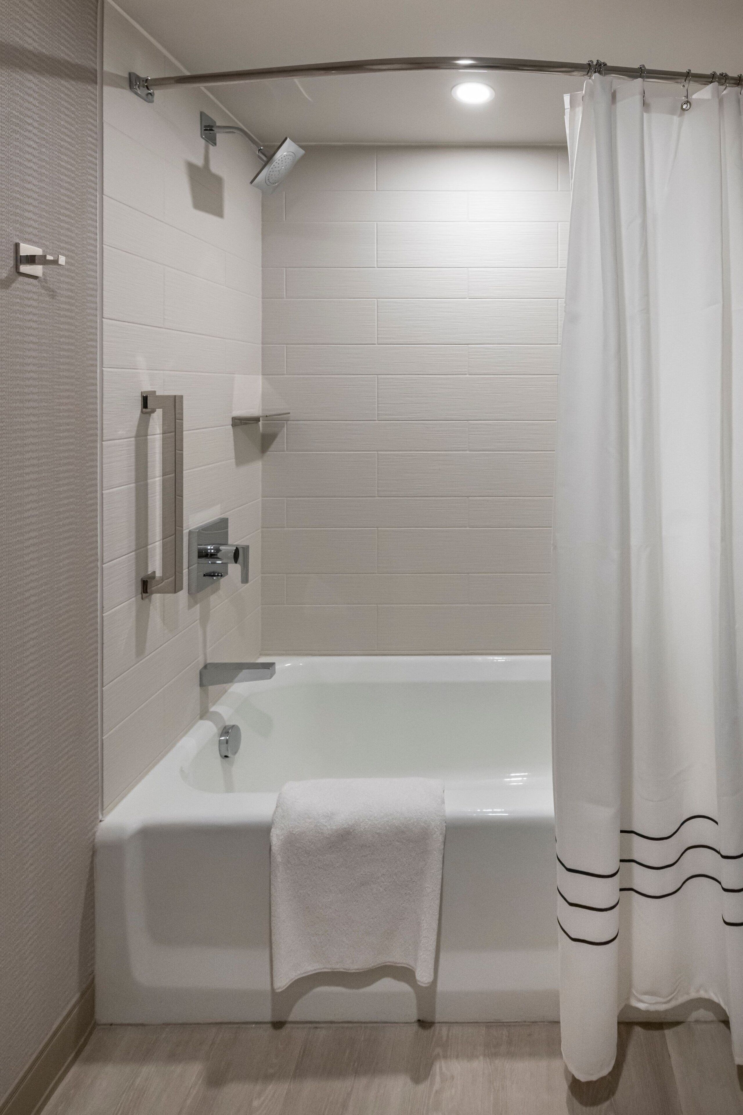 A modern bathroom with a white bathtub, a showerhead, and a white curtain.