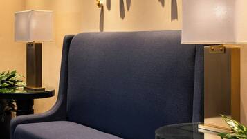 Un sofá azul en una habitación de hotel con una alfombra estampada, dos mesitas de noche con lámparas y un aplique en la pared.