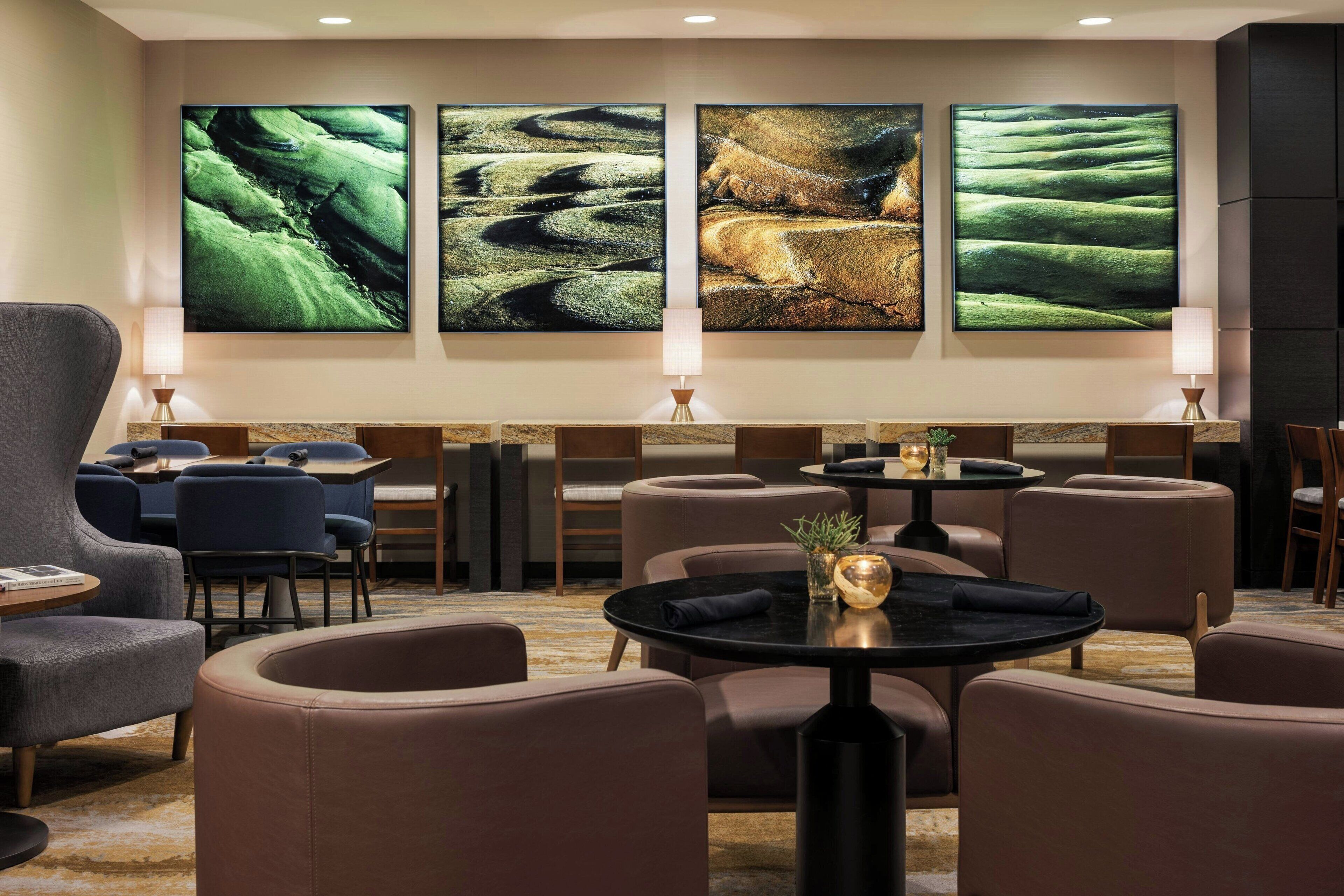A hotel lobby with a seating area, tables, and three large wall-mounted artworks.