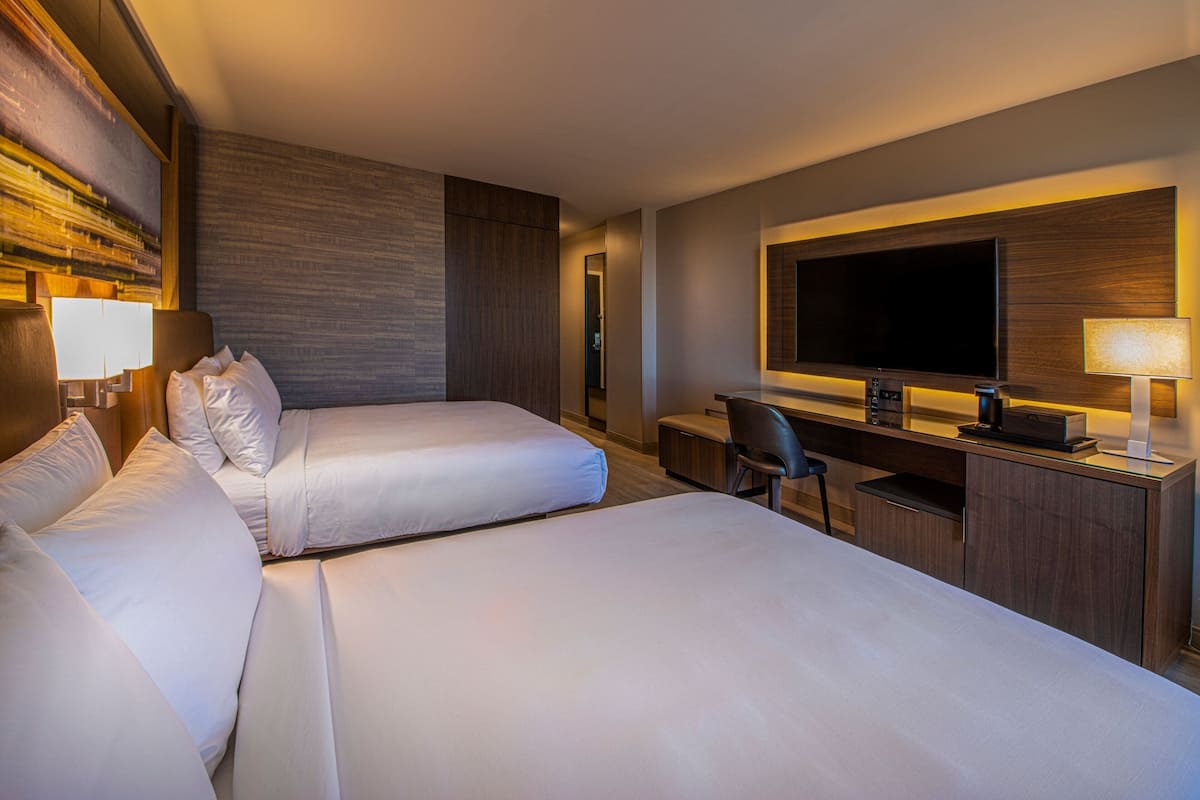 A hotel room with two beds, a desk, a chair, a television, and a large mirror.