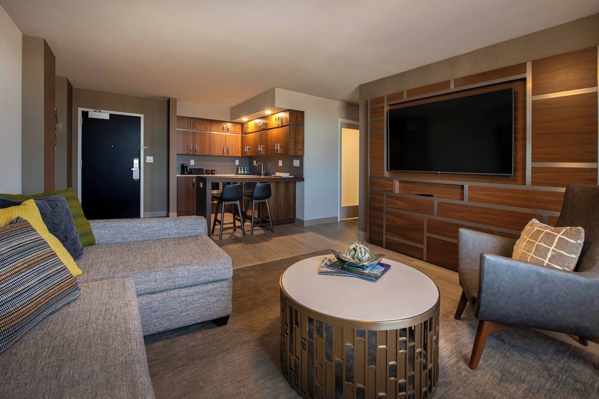 A modern living room with a sofa, armchair, coffee table, and a TV mounted on the wall.