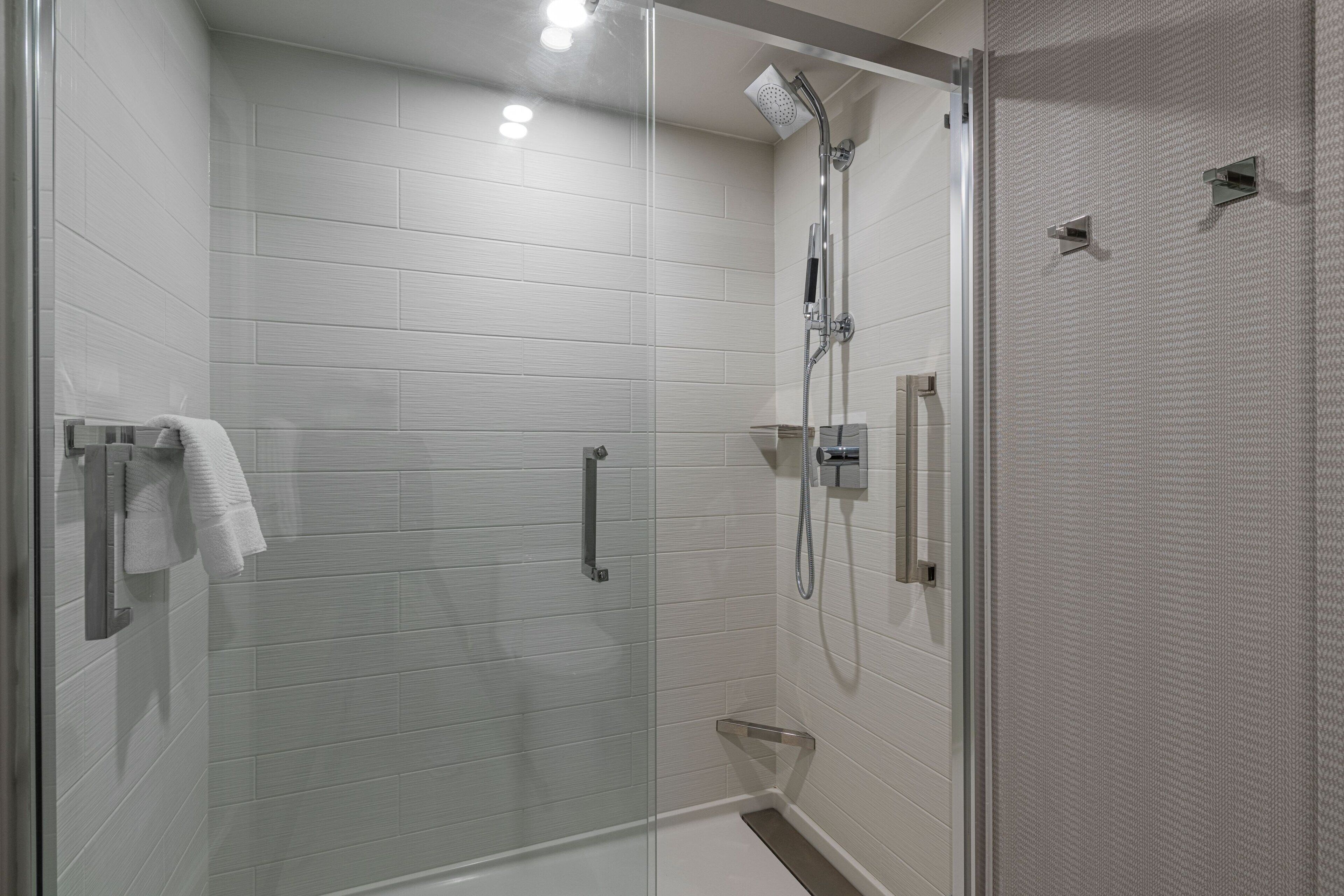 A modern shower area with a glass door, white tiled walls, and a handheld showerhead.