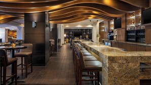 A modern bar area with a long counter, bar stools, and a television screen. - Marriott Wichita (Wichita)