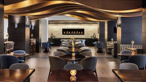 A modern restaurant with a central fireplace, dark wood paneling, and contemporary seating. - Marriott Wichita (Wichita)